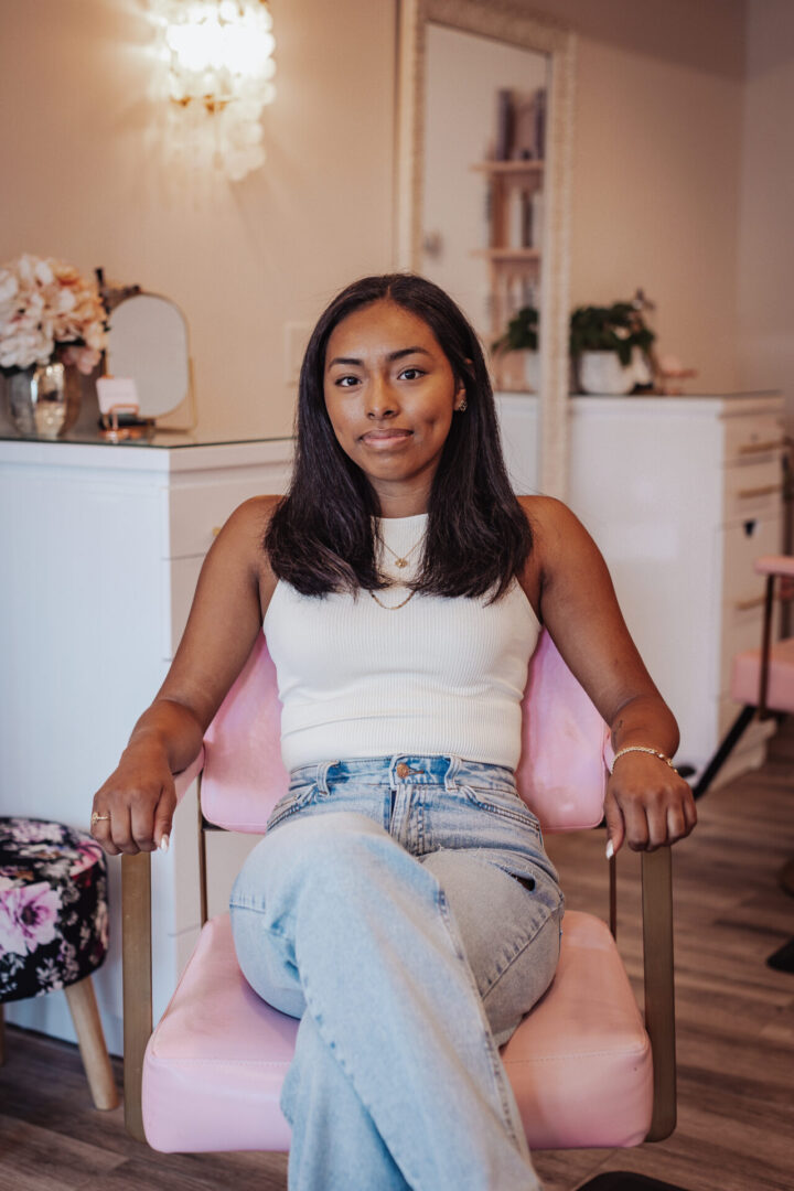 A woman sitting in a chair wearing jeans and white top.
